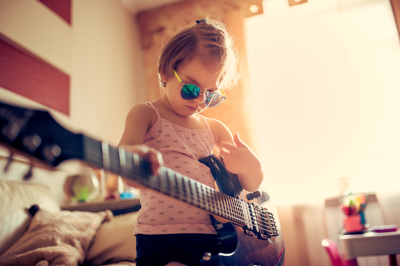 Cute little child girl in sunglasses playing guitar at home